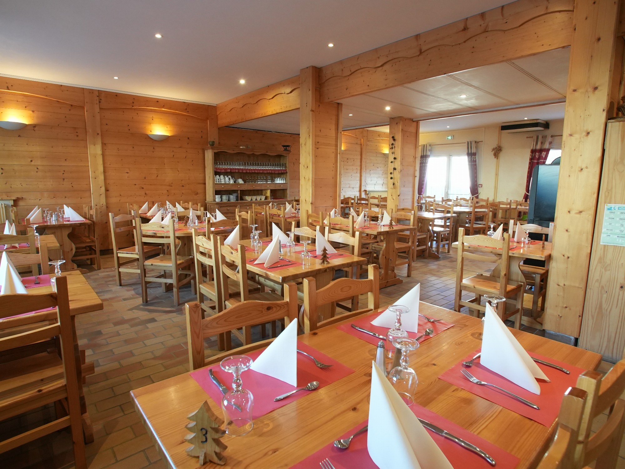 Tables dressées dans un cadre entièrement en bois, éclairage assuré par des appliques murales et des luminaires encastrés au plafond. Les tables sont numérotées avec de petits sapins en bois avec la table n°3 au premier plan