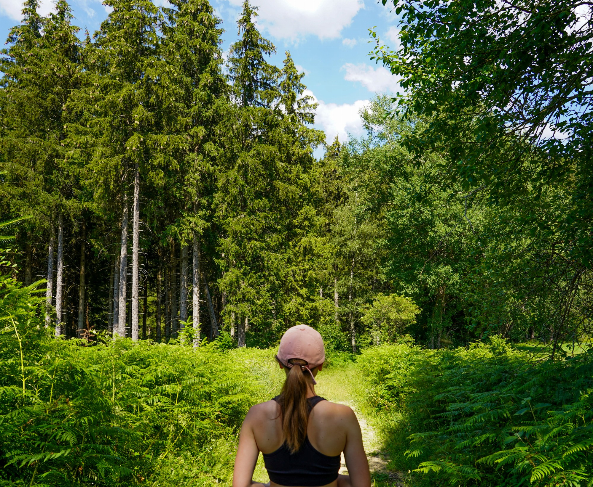 Femme marchant sur le sentier entourée de sapins.