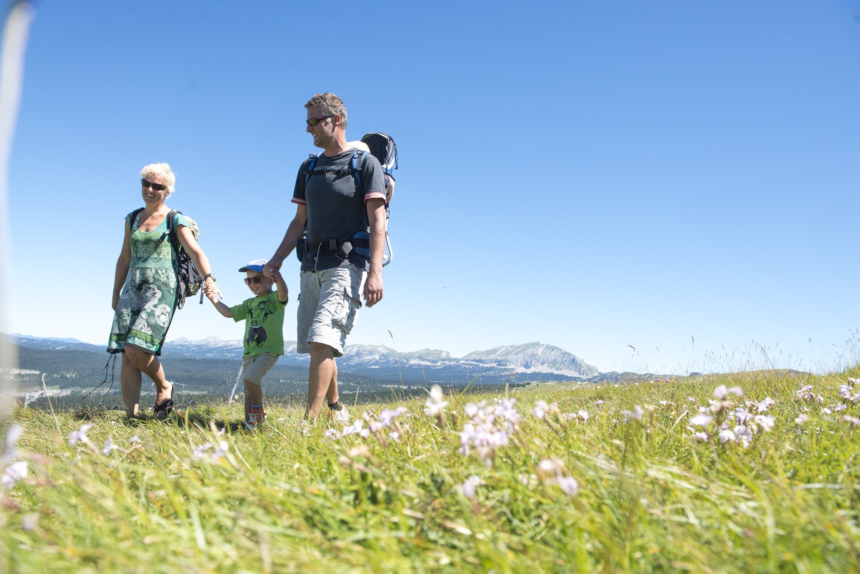 Couple avec enfant marchant dans une prairie avec le Grand Veymont en arrière plan