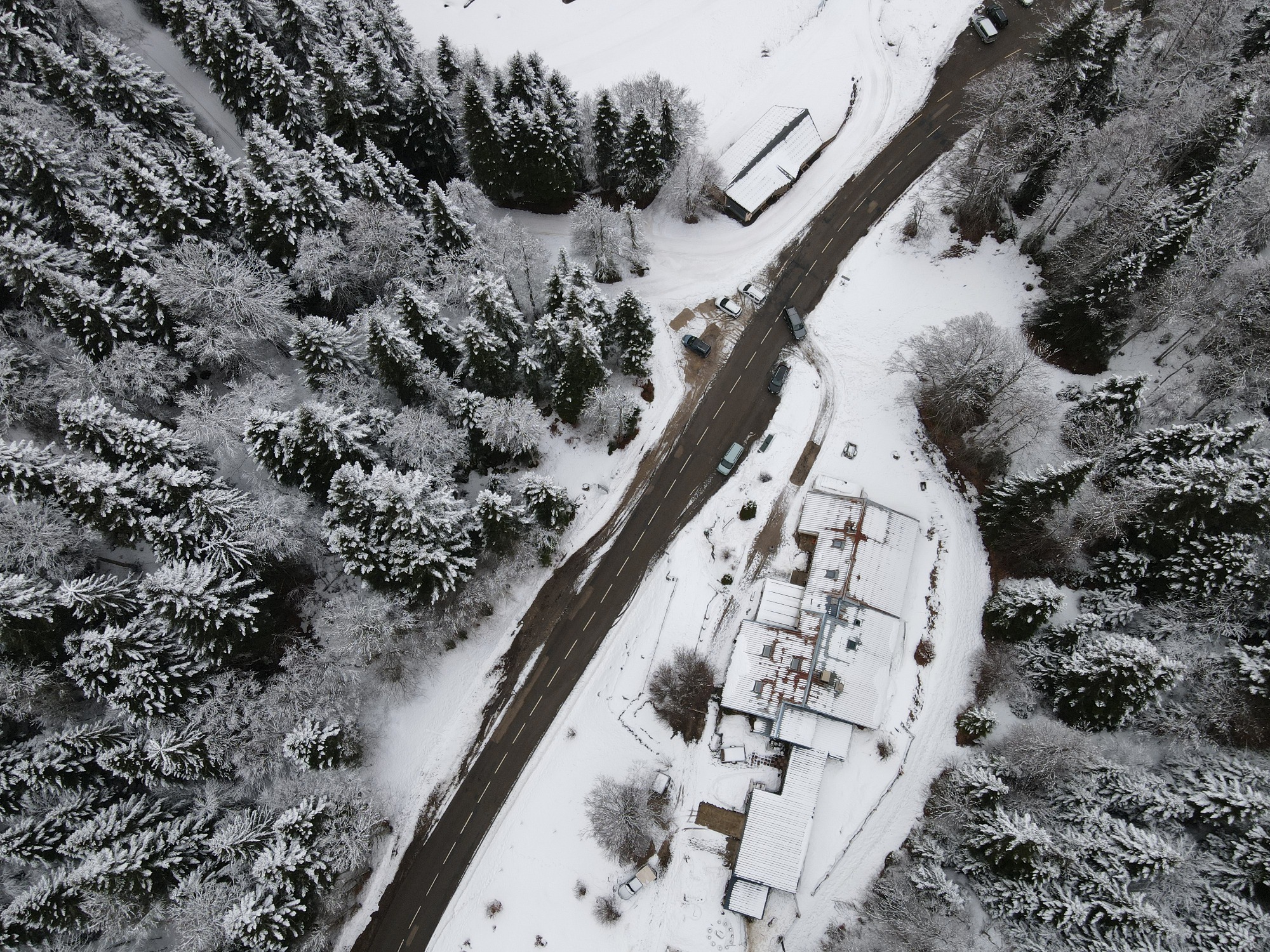 Vue drone du gîte et auberge de Carri à La Chapelle en Vercors, avec la route enneigée qui serpente à travers une forêt hivernale,.